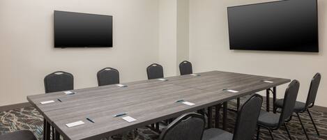 A conference room with a long table, multiple chairs, and two mounted TVs on the walls.