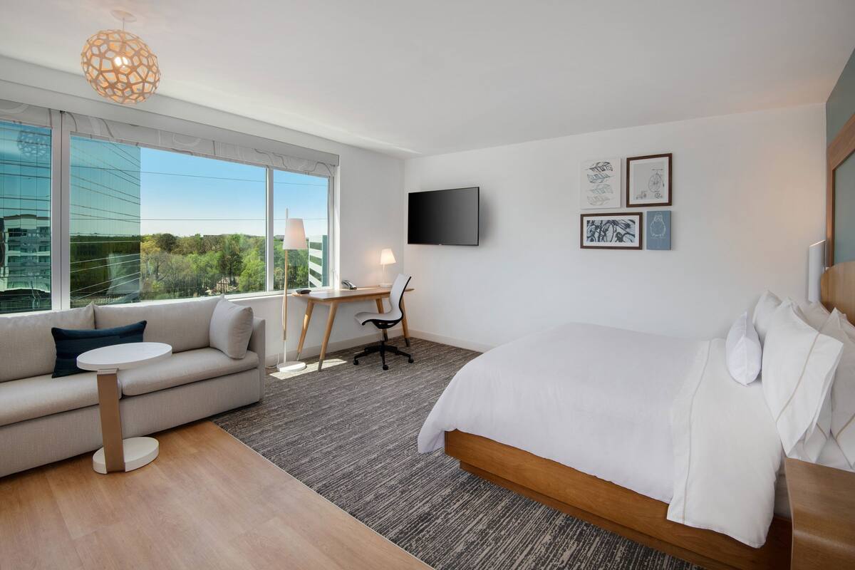 A modern hotel room with a large bed, a sofa, a desk, and a TV.