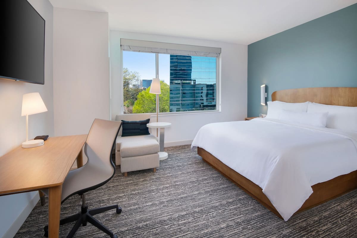 A hotel room with a large bed, a desk with a chair, a small table, and a TV mounted on the wall.