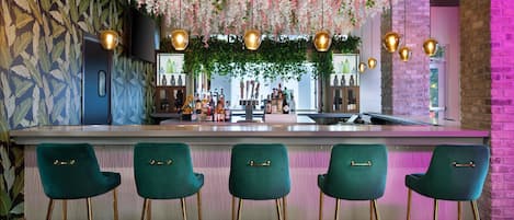 A bar area with a counter, green bar stools, hanging floral decorations, and pendant lights.