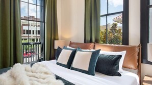 A hotel room with a large bed, green curtains, and a view of buildings outside.