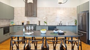 A modern kitchen with grey cabinets, a large island with chairs, stainless steel appliances, and pendant lighting.