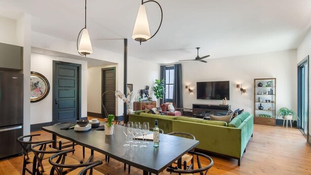 A modern living space with a dining area, green sofa, and a flat-screen TV.