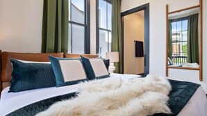 A hotel room with a bed, green curtains, a wooden headboard, and a view of the outside through the window.