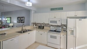 Una cocina moderna con gabinetes blancos, microondas, estufa y refrigerador.