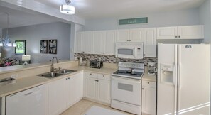 A modern kitchen with white cabinets, a microwave, a stove, and a refrigerator.