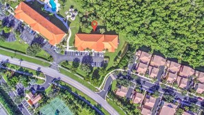 Vista aérea de una zona residencial con piscina, cancha de tenis y un edificio de techo rojo.