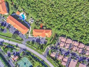 An aerial view of a residential area with a swimming pool, a tennis court, and a red-roofed building.