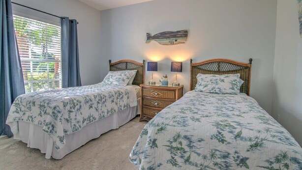 A bedroom with two beds, a nightstand with a lamp, and a wall-mounted artwork.