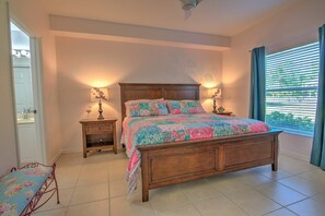 A bedroom with a wooden bed, two bedside tables, a window with curtains, and a door leading to another room.