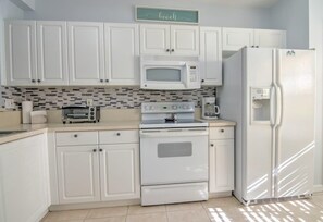 A kitchen with white cabinets, a microwave, a stove, and a refrigerator.