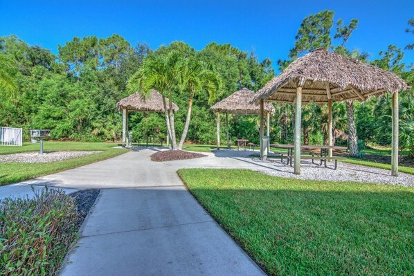 A park with thatched-roof gazebos, a paved walkway, and well-maintained grassy areas.