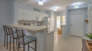 A kitchen with white cabinets, a central island with bar stools, a microwave, and a refrigerator.