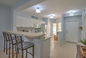A kitchen with white cabinets, a central island with bar stools, a microwave, and a refrigerator.