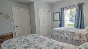 Un dormitorio con dos camas, paredes blancas, una ventana con cortinas y una puerta.