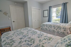 A bedroom with two beds, white walls, a window with curtains, and a door.