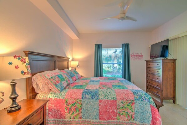 A bedroom with a bed, a dresser, a television, and a window with curtains.
