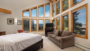 A bedroom with a large bed, a sofa, a TV, and multiple windows offering a view of trees and mountains. - Beautiful home in Fraser with great breathtaking views and private hot tub (Fraser)