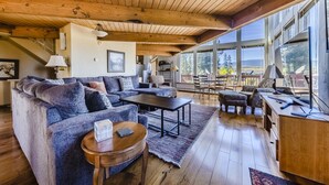 A spacious living room with a wooden ceiling, large windows, a sofa, a coffee table, and a desk area. - Beautiful home in Fraser with great breathtaking views and private hot tub (Fraser)