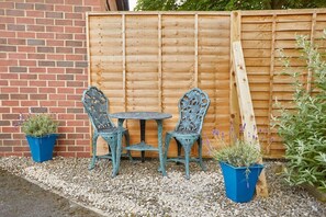 A patio with a wooden fence, two chairs, a small table, and two potted plants. - Host & Stay | The Limes (Harrogate)