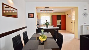 A modern dining area with a black and white table, surrounded by black chairs. A fruit bowl with bananas and pineapples is on the table. The kitchen in the background has red cabinets and a white countertop. - Relaxing rural apartment with playground and grill (Nedescina)