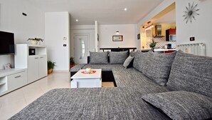 A modern living room with a grey sofa set, a white coffee table, and a flat-screen TV on a white cabinet. - Relaxing rural apartment with playground and grill (Nedescina)