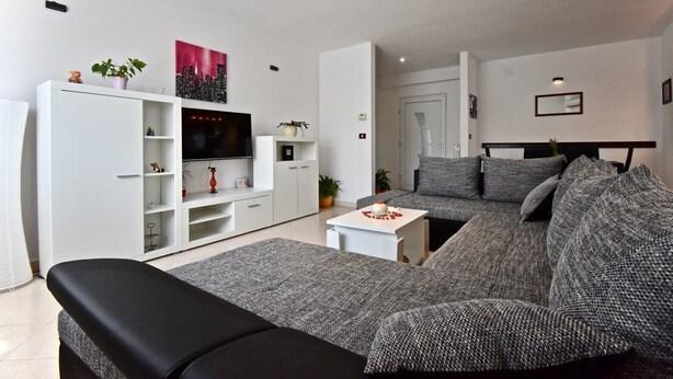 A modern living room with a sectional sofa, a flat-screen TV, and a white entertainment unit. - Relaxing rural apartment with playground and grill (Nedescina)
