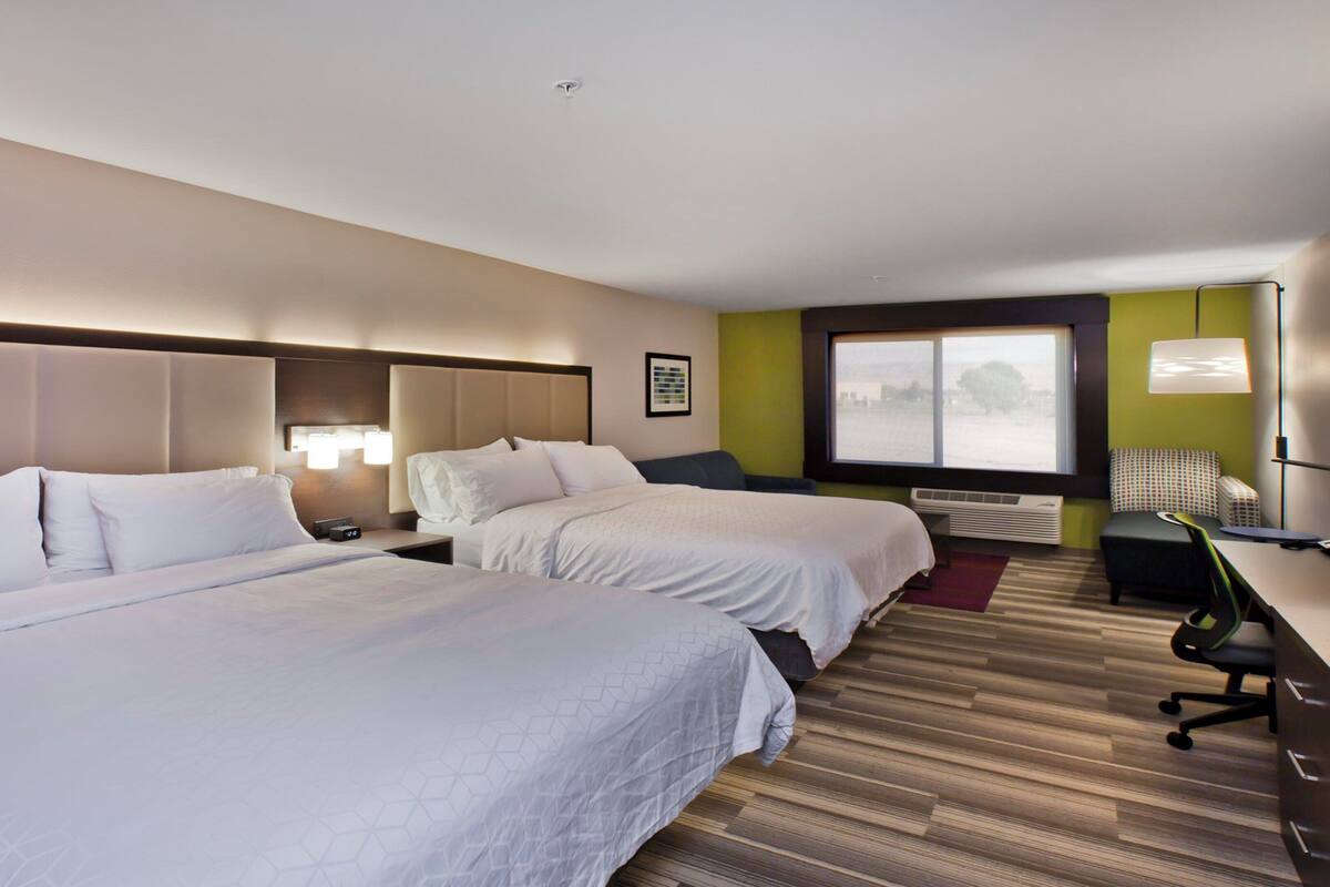 Une chambre d’hôtel avec deux lits, un bureau, une chaise, une fenêtre et un climatiseur fixé au mur.