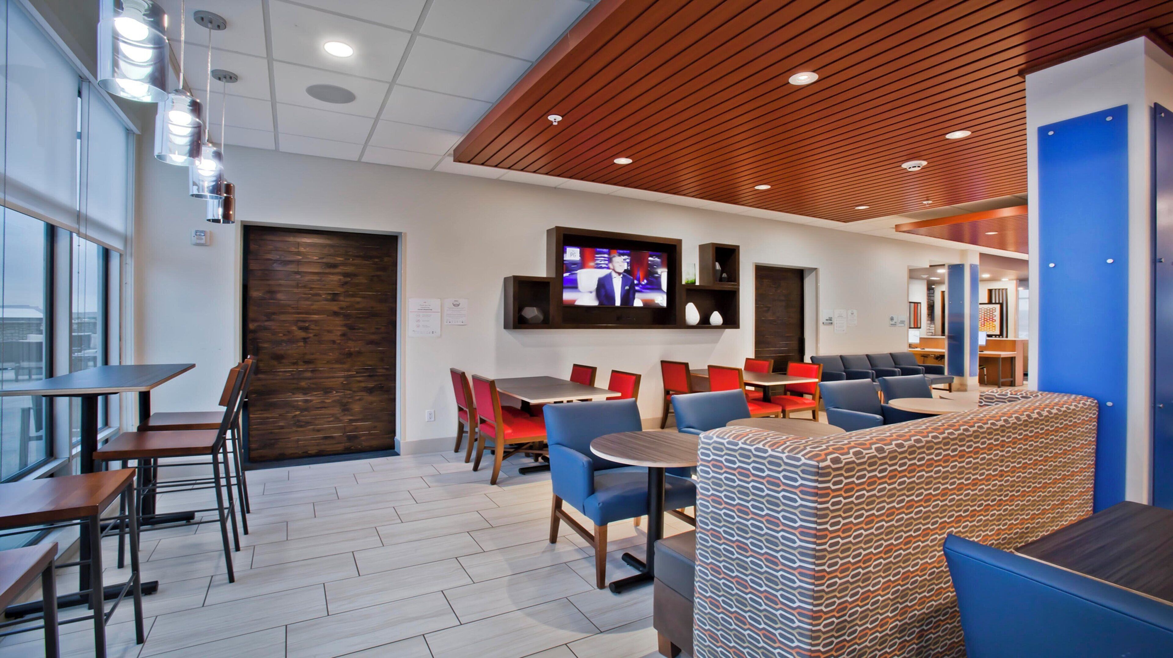 A modern hotel lobby with a TV, seating areas, and a wooden ceiling.