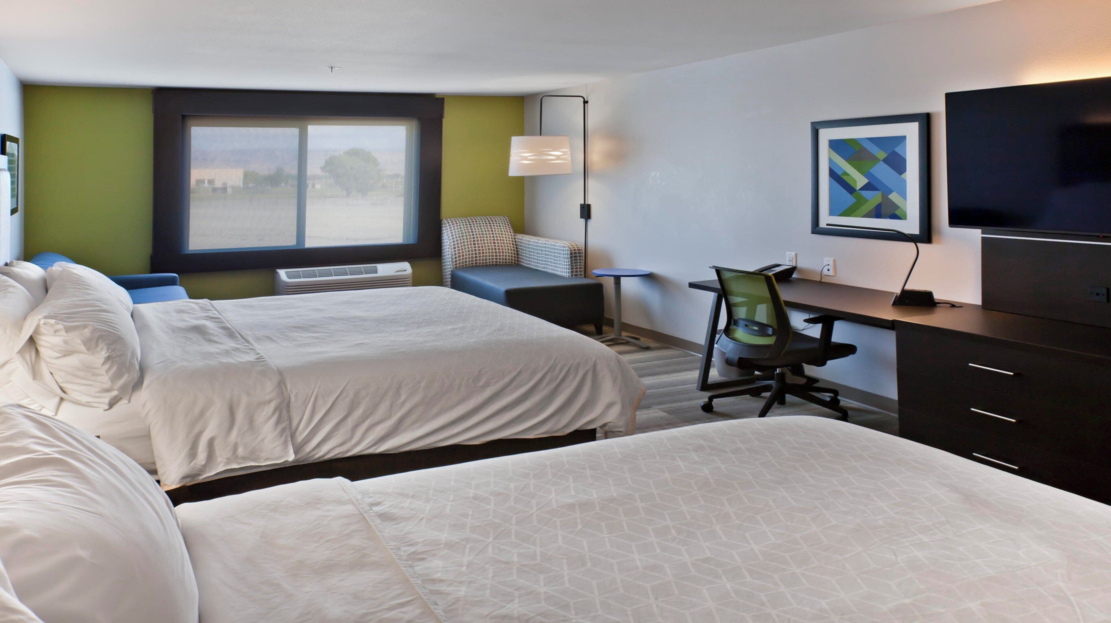A hotel room with two beds, a desk, a chair, a TV, and a window with a view.