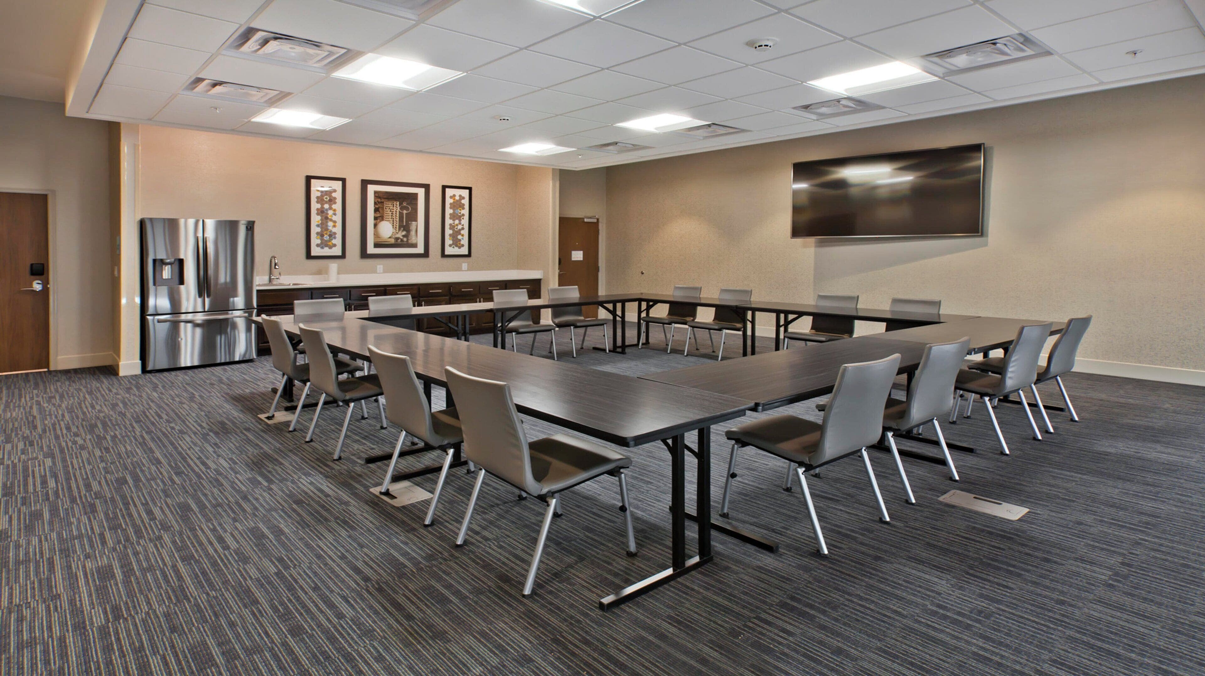 A conference room with a long table, chairs, a refrigerator, and framed artwork on the wall.