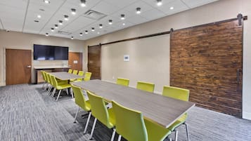 A conference room with a long table, yellow chairs, a projector screen, and a wooden panel wall.