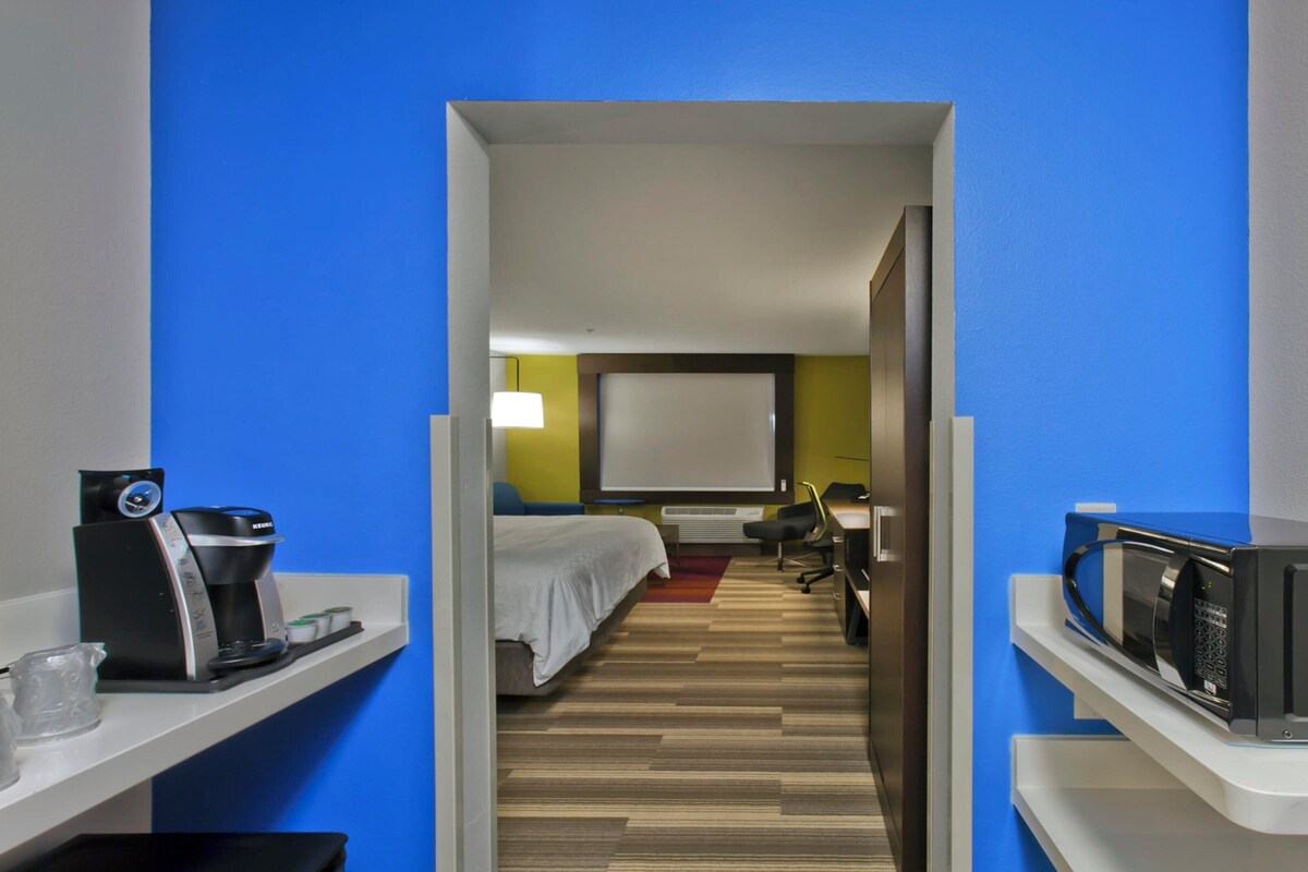 A hotel room with a bed, a desk, a microwave, and a coffee machine.