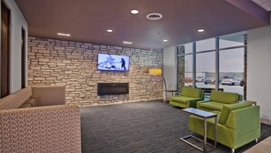 A modern lounge area with a stone wall, a flat-screen TV, green chairs, and a view of a parking lot through large windows. - Holiday Inn Express & Suites Green River by IHG (Green River)