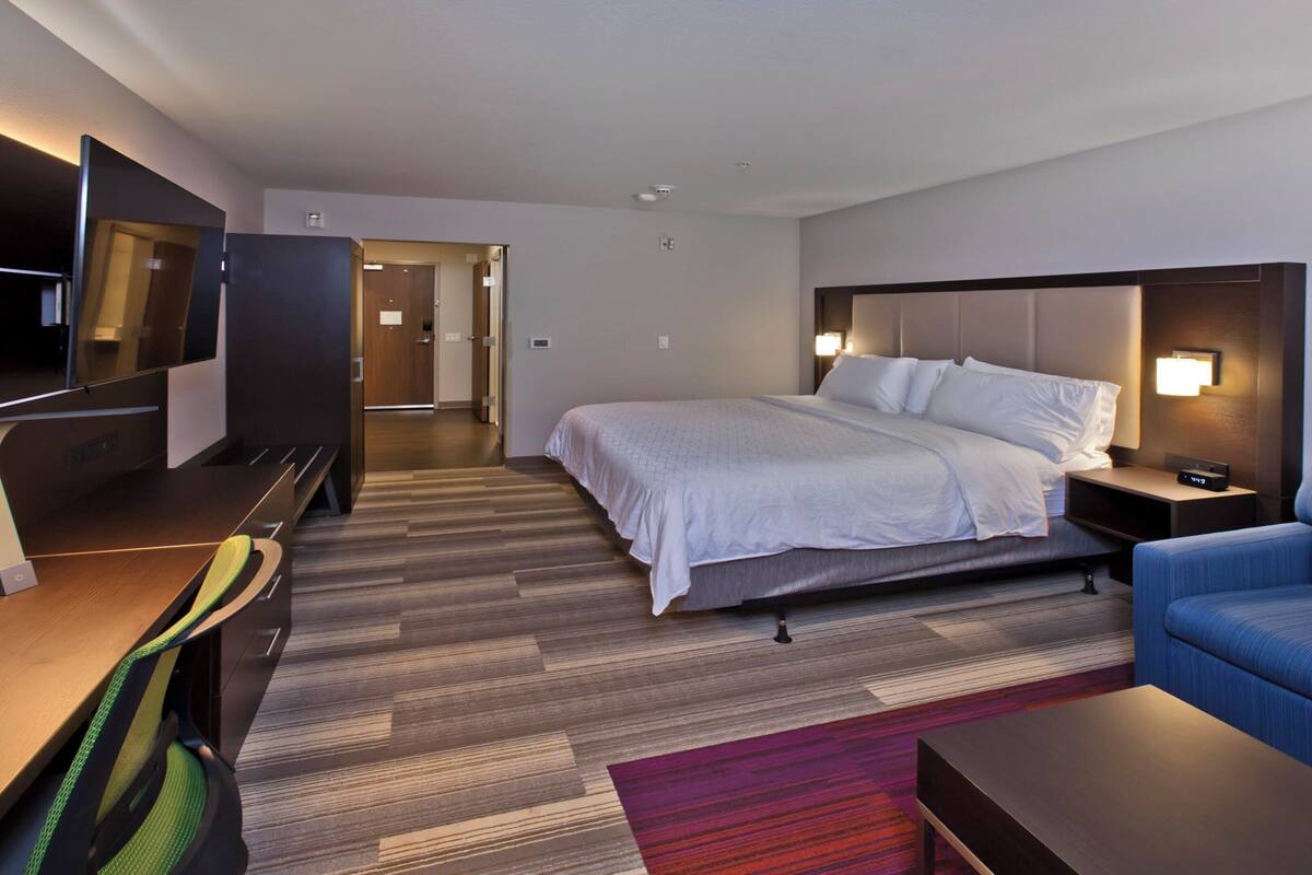 Une chambre d’hôtel avec un lit, un bureau avec un ordinateur, une télévision, un canapé bleu et un tapis rouge.