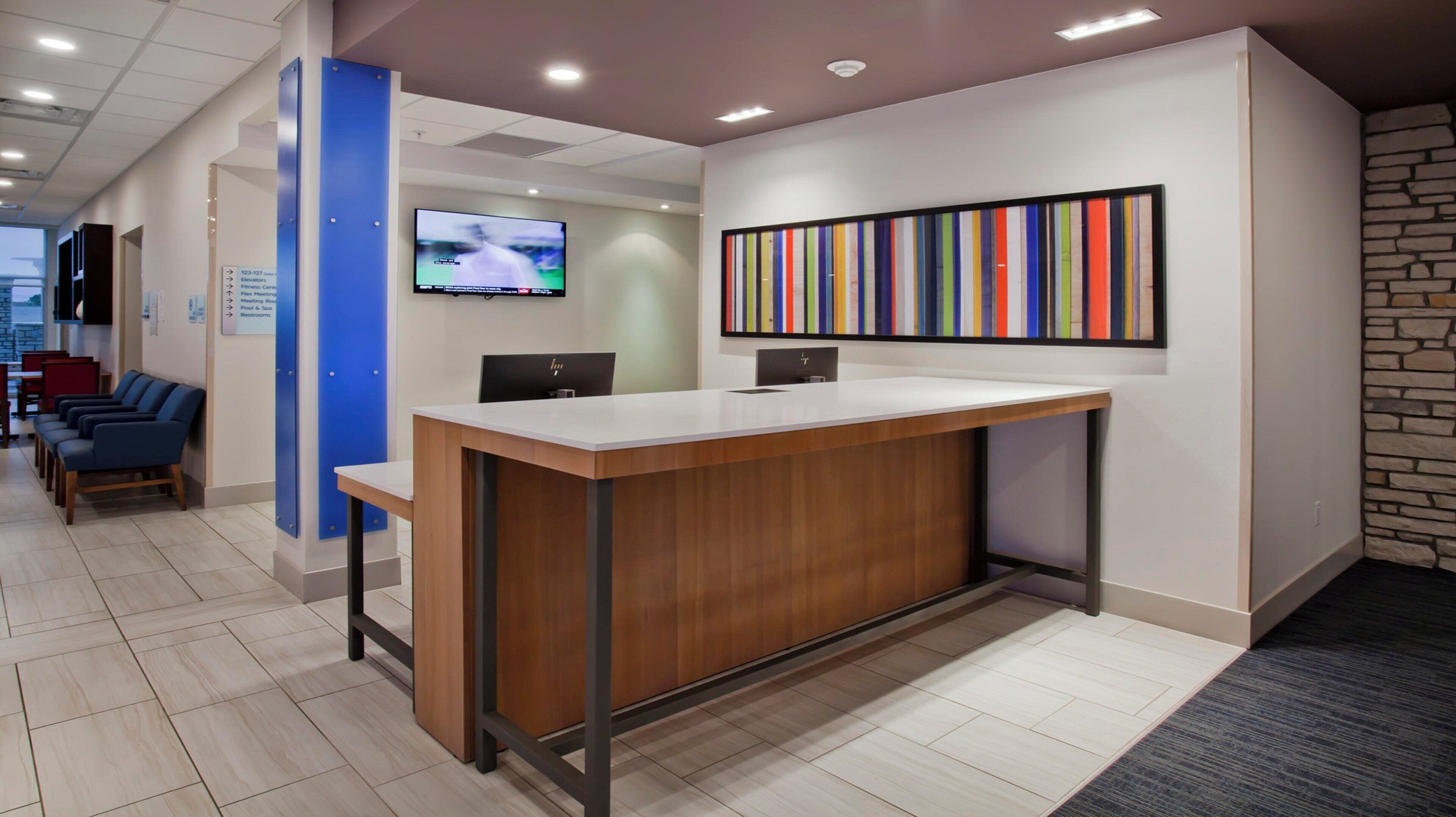 A reception area with a wooden reception desk, a TV mounted on the wall, and a colorful striped artwork above the desk.