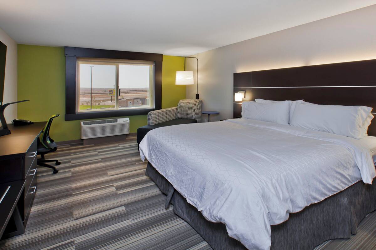 Une chambre d’hôtel dotée d’un grand lit, d’un bureau, d’une chaise, d’une fenêtre avec vue et d’une tête de lit pourvue d’un éclairage intégré.