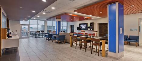 A modern hotel lobby with a bar area, seating, and a large TV screen.