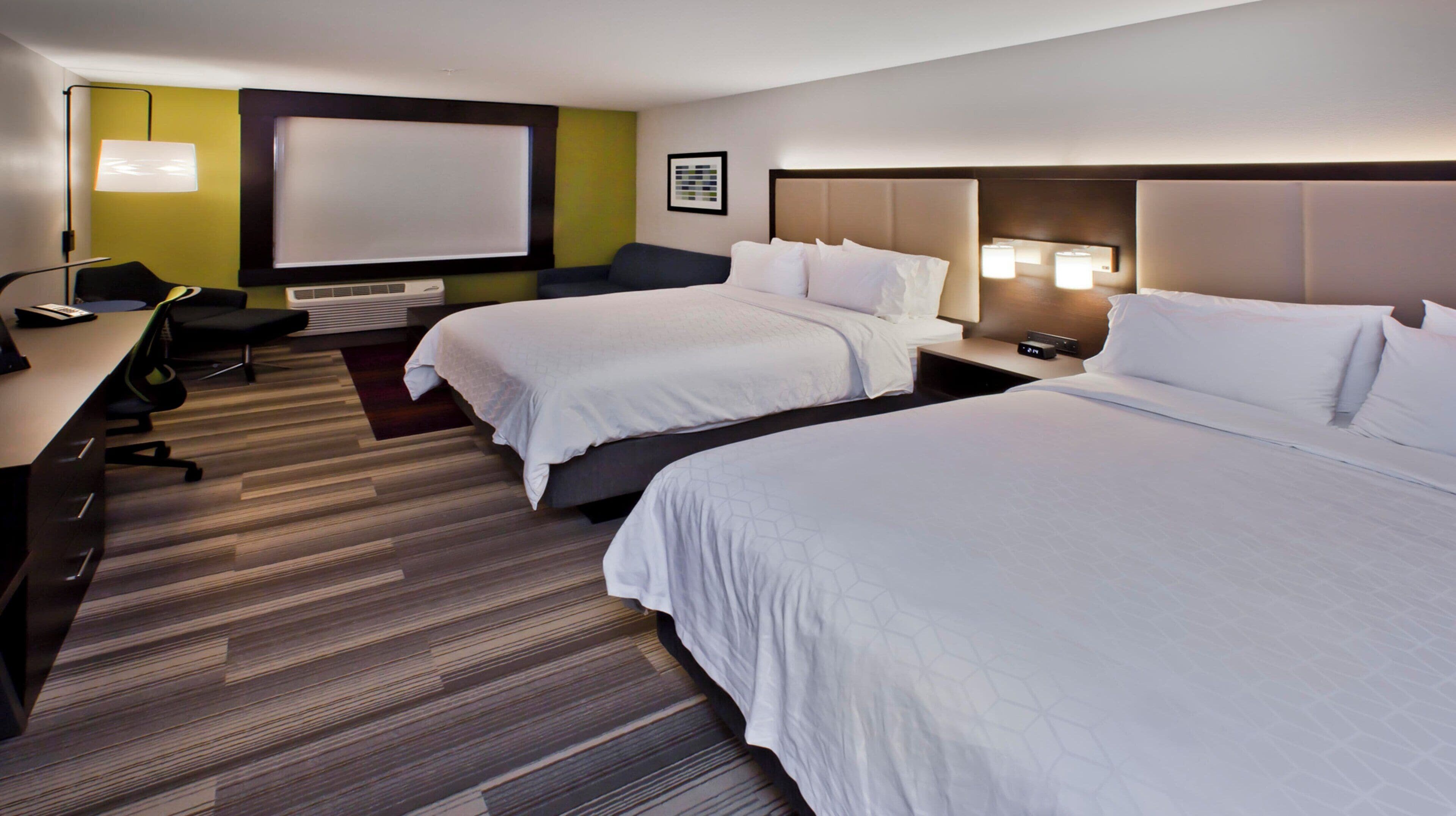 Une chambre d’hôtel avec deux lits, un bureau, une chaise, une lampe et une grande fenêtre.
