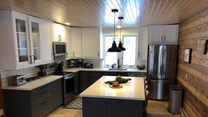 Une cuisine moderne avec des meubles blancs, un îlot central, des appareils en acier inoxydable et des luminaires suspendus.