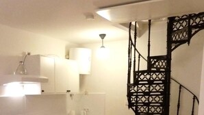A compact kitchen with white cabinetry, a built-in oven, and a sink. A staircase with intricate black railings leads to an upper level.