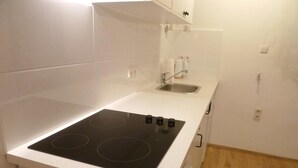 A compact kitchen with a black stovetop, a stainless steel sink, and white cabinetry.