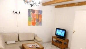 Ein Wohnzimmer mit einem beigen Sofa, einem Couchtisch aus Holz mit Zeitschriften, einem Fernseher auf einem Holzschrank und einem farbenfrohen abstrakten Gemälde an der Wand.