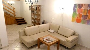 Ein Wohnzimmer mit einem beigefarbenen Ecksofa, einem Holztisch, einer Treppe mit Holzhandläufen und einem farbenfrohen abstrakten Gemälde an der Wand.