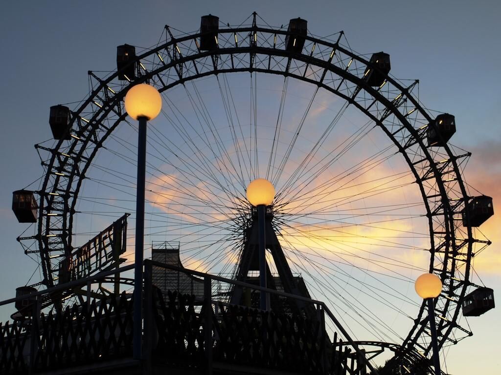 Une grande roue au crépuscule, avec un coucher de soleil en arrière-plan.