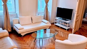A modern living room with a sofa, armchairs, a glass coffee table, and a flat-screen TV.