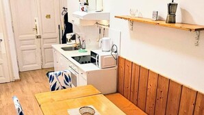 A dining area with a wooden table and chairs, a kitchen in the background, and a wooden bench along the wall.