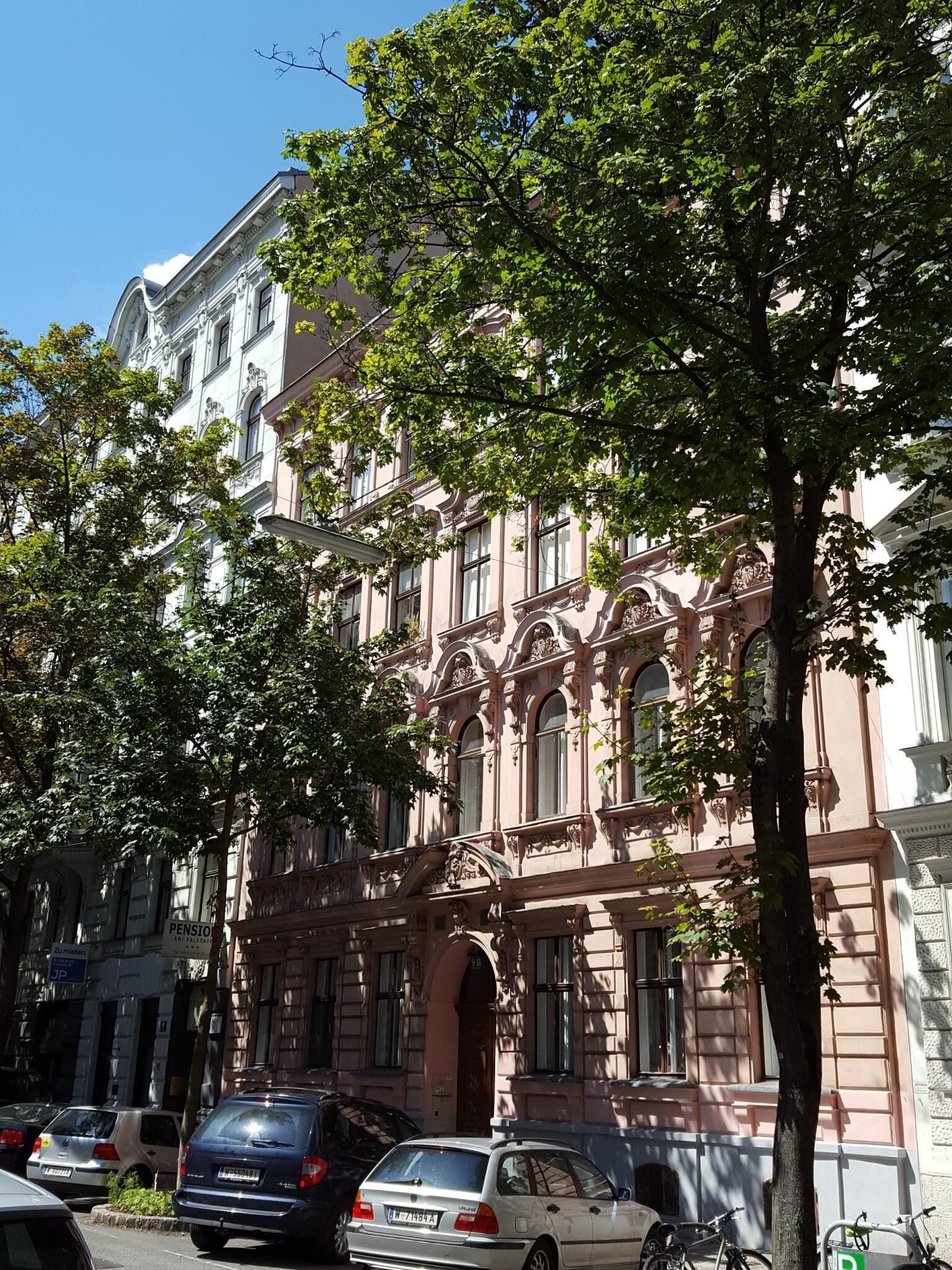 A historic building with ornate architecture, parked cars, and a tree in front.