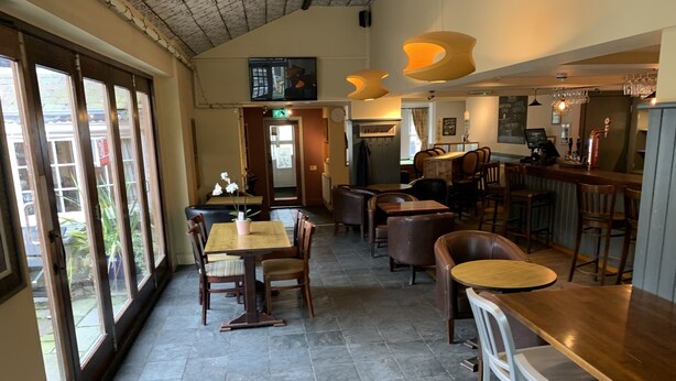 A restaurant interior with high ceilings, large windows, and a mix of wooden and metal furniture. - George & Dragon (Chester)