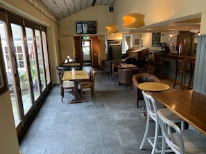 A restaurant interior with high ceilings, large windows, and a mix of wooden and metal furniture.